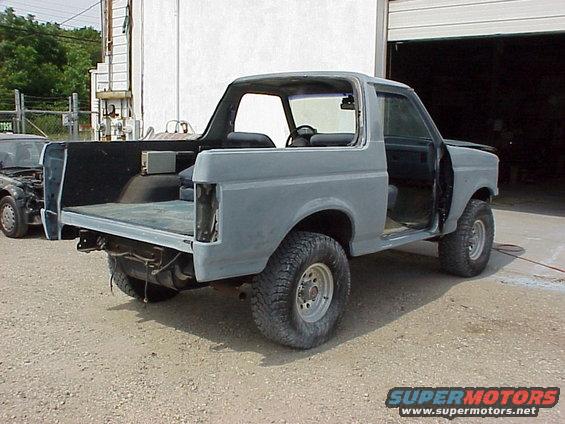 Gray SUV in primer, doors open, rear cargo area exposed. Another vehicle visible to the left
