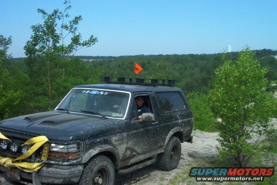 1993 Ford Bronco with hood scoop and roof rack driving off-road, yellow tow strap on front bumper