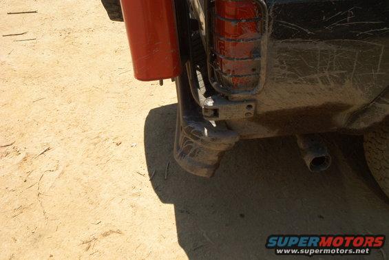 Rear bumper, taillight, and exhaust pipe of a vehicle parked on dirt