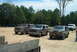 1993 Ford Bronco - Several Ford Broncos and a van are parked on a dirt lot with trees and a blue sky overhead.