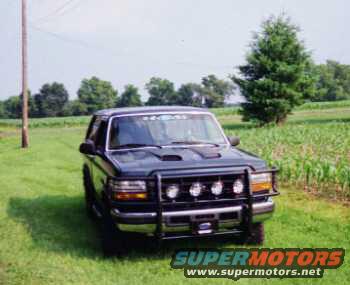 Dark-colored Ford Bronco parked in a grassy field with trees in the background