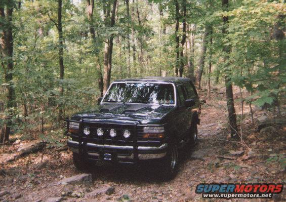 Dark green 1993 Ford Bronco with bull bar and auxiliary lights on wooded trail