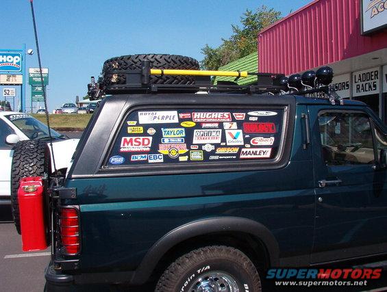 Dark green SUV side view with roof rack, spare tire, and numerous stickers on rear window