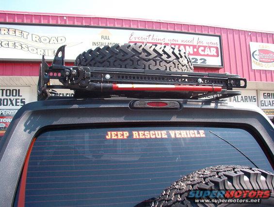 Rear of a Jeep with a roof rack holding a spare tire and a Hi-Lift jack. 'JEEP RESCUE VEHICLE' sticker on the rear window