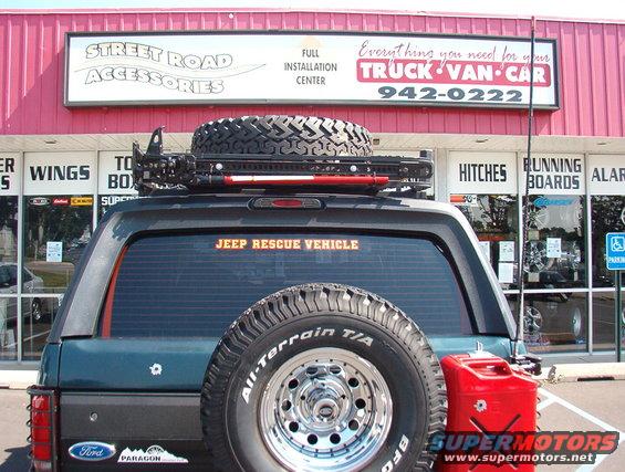 1993 Ford Bronco rear view, dark green, with spare tire on roof rack and rear door, red jerry can on right