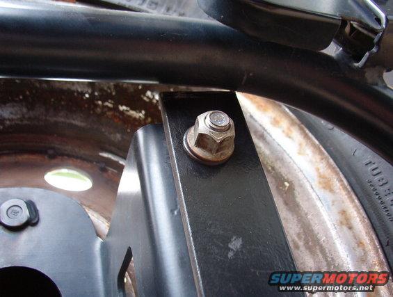 Metal bracket bolted to a rusty wheel rim with a black tube above