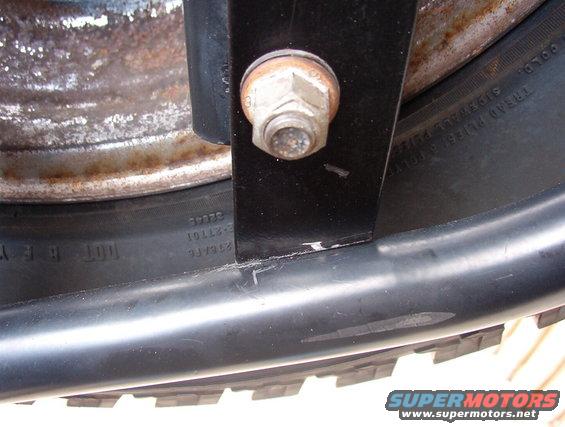 Close-up of a spare tire with visible sidewall text and a black mounting bracket with a bolt