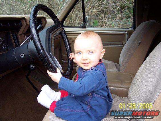 Baby in a car seat, holding onto the steering wheel