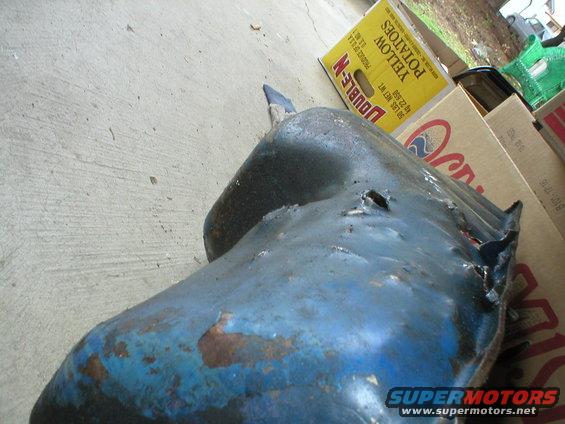Blue metal oil pan with rust and a hole in it, sitting on concrete. Boxes are in the background