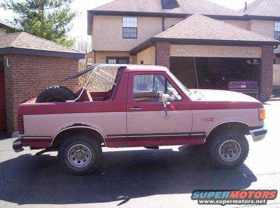 Side view of a red and tan 1989 Ford Bronco with a spare tire in the bed