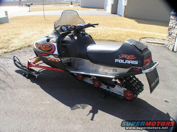 Polaris 500 XC SP snowmobile parked on asphalt. Has red front suspension and black seat with XC logo