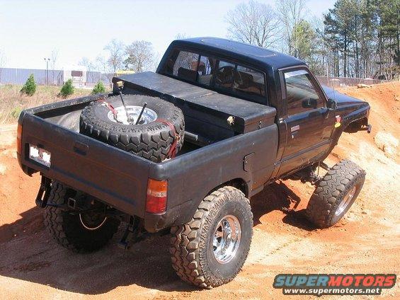 Black lifted pickup truck with a spare tire in the bed, driving on a dirt track