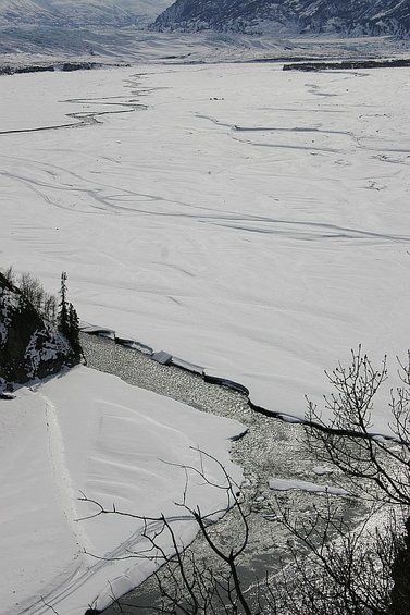 Frozen river with ice floes and snow-covered banks, distant mountains under a cloudy sky