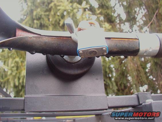 Close-up of a roof rack bar secured with a padlock. Water droplets are visible on the bar