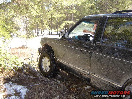 Black SUV with mud splatters, off-road tires, driving on a dirt path with trees and snow