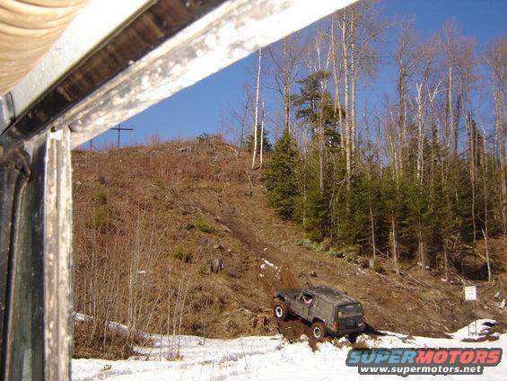 Jeep Cherokee XJ climbing a muddy hill with trees and snow around