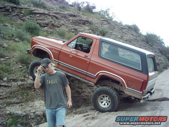 Orange Ford Bronco with black top on a dirt hill, person standing nearby