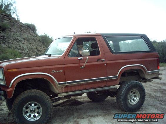 Red Ford Bronco with a black top, lifted suspension, and off-road tires, seen from the side