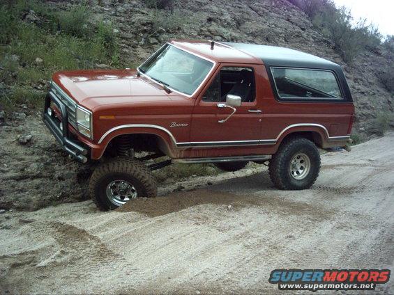 Red Ford Bronco with black top, lifted suspension, off-roading on a dirt path