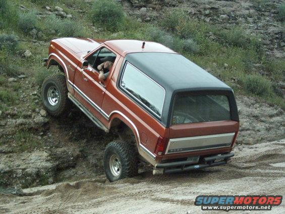 Orange SUV with black top on a dirt trail, driver visible