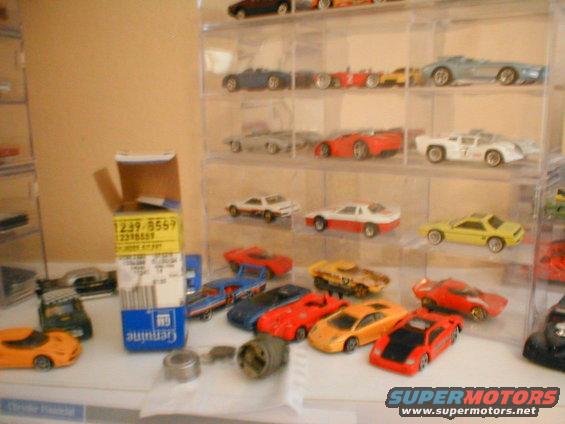 Collection of toy cars on shelves and a table, with a box of parts