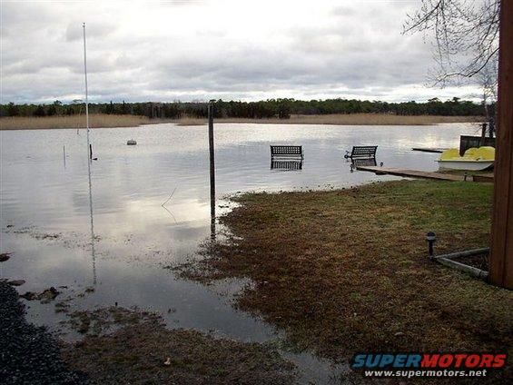 Flooded yard with two benches partially submerged in water. A yellow boat is docked on the right