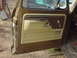 1979 Ford Bronco - The interior door panel of a 1979 Ford Bronco shows its brown and tan trim, with a manual window crank.