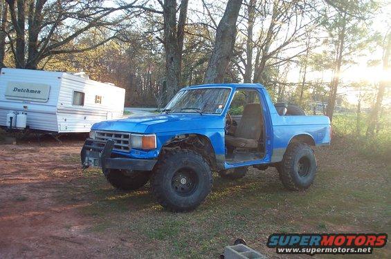 Blue pickup truck with large off-road tires and no doors parked next to a white camper trailer