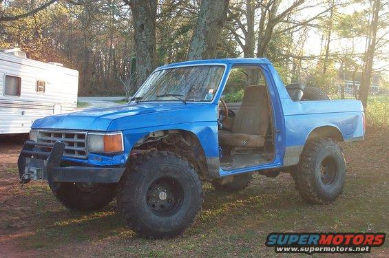 Blue off-road SUV with large tires, missing doors, and a brush guard