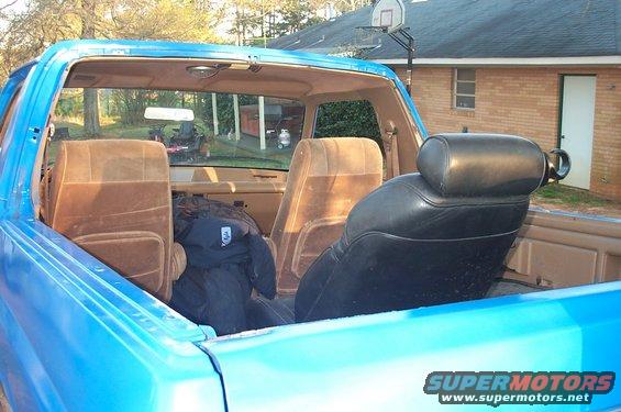 Interior view of a blue Ford Bronco, showing brown cloth seats and a black leather seat. A jacket is on the back seat