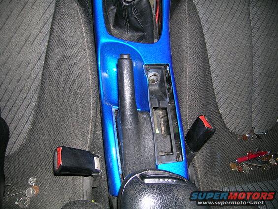Car's center console with blue trim, handbrake, and gear shifter removed. Seatbelts and coins visible