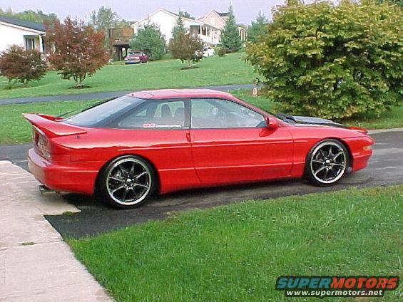 Red 1994 Ford Probe coupe with aftermarket wheels and spoiler, parked on a driveway
