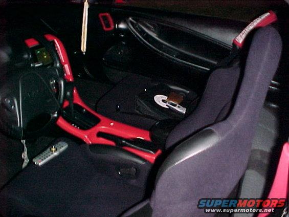 Car interior with red accents on the center console and dashboard, dark seats, and a remote control on the floor