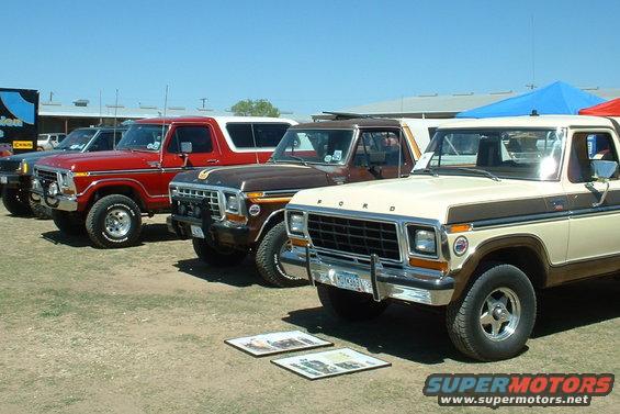 Several Ford Broncos and F-Series trucks parked in a row on a sunny day. The closest vehicle is a tan and brown F-Series truck