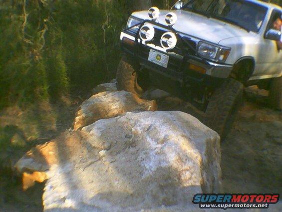 White SUV with off-road lights driving over large rocks