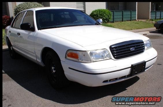 White Ford Crown Victoria parked on asphalt, front quarter view. Black grille with Ford logo