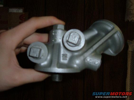 Silver metal engine oil filter housing held in a hand, with "FORD" visible on the part