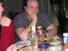 1984 Ford Bronco - A group of people are gathered around a table laden with food and drinks, with one man appearing disengaged from the conversation.