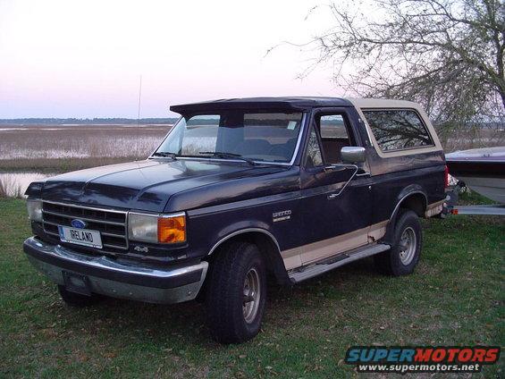 Dark blue and tan Ford Bronco with a tan removable top parked on grass near water