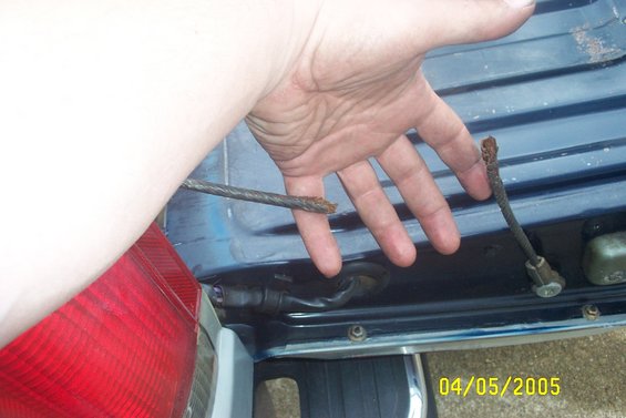Blue vehicle door with a hand holding a frayed cable, red taillight visible