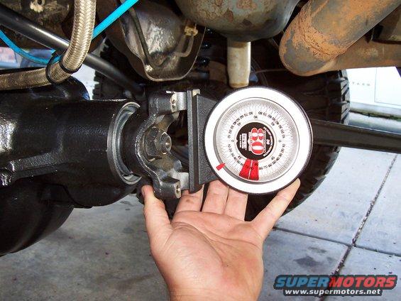 Hand holding angle gauge against automotive differential housing. SuperMotors.net logo visible