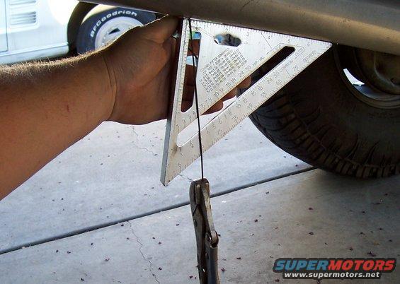 Hand holding a speed square and plumb bob to measure vehicle frame