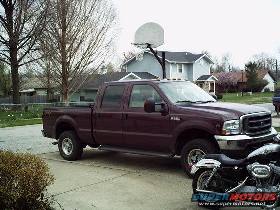 Maroon Ford F-250 Super Duty pickup truck parked on a driveway next to a motorcycle