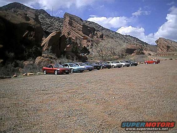Several cars parked in a row with red rock formations in the background
