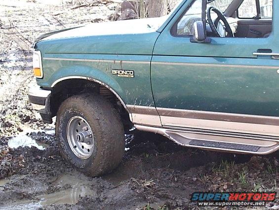 Green 1996 Ford Bronco with a "BRONCO" badge on the fender stuck in mud, showing the front wheel and side door