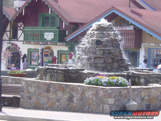 Stone fountain with cascading water and flowers in front of Bavarian-style buildings