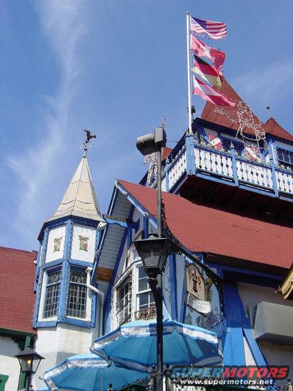 Building with red roof, blue trim, and flags flying from a pole against a blue sky