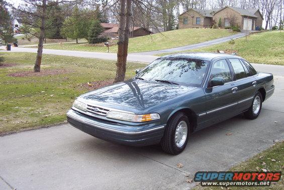 Green Ford Crown Victoria sedan parked on driveway, front quarter view