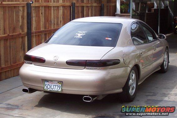 Tan sedan's rear view, showing dual exhaust tips, Mercury badging, and a California license plate