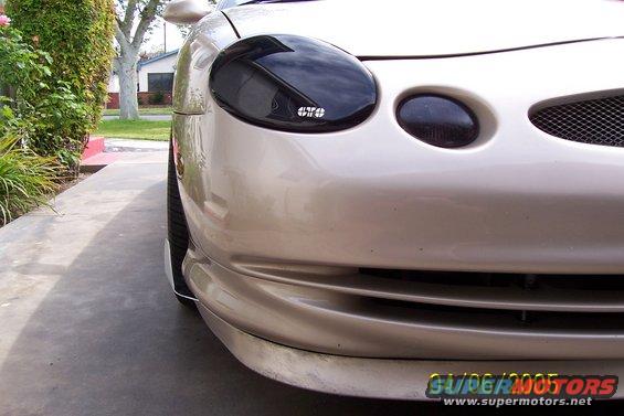 Car front with dark headlights and a mesh grille. Some text on the headlight says 'OTO'